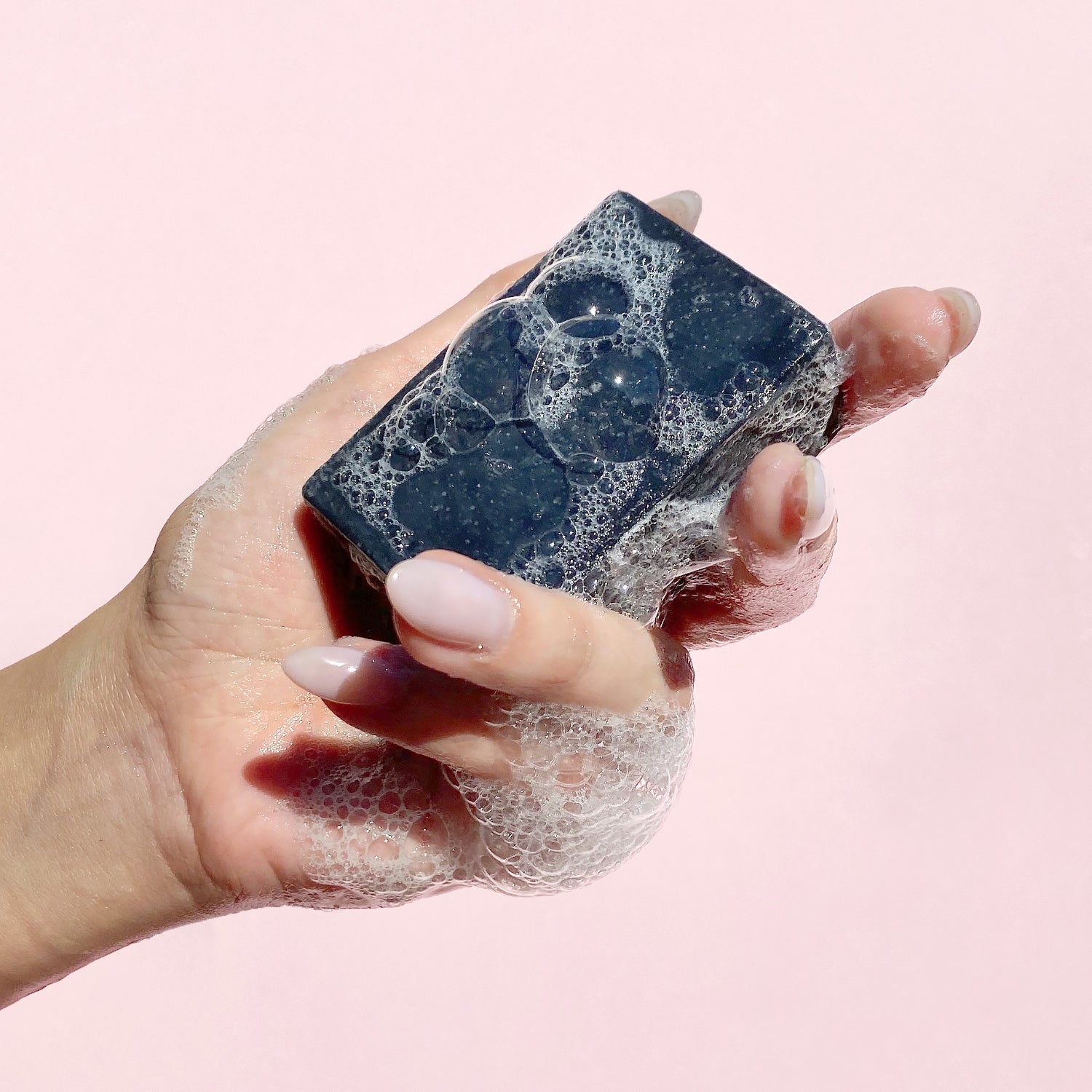 A hand holding a foaming bar of BAMBOO CHARCOAL Cleansing Bar Soap | Herbivorebotanicalss